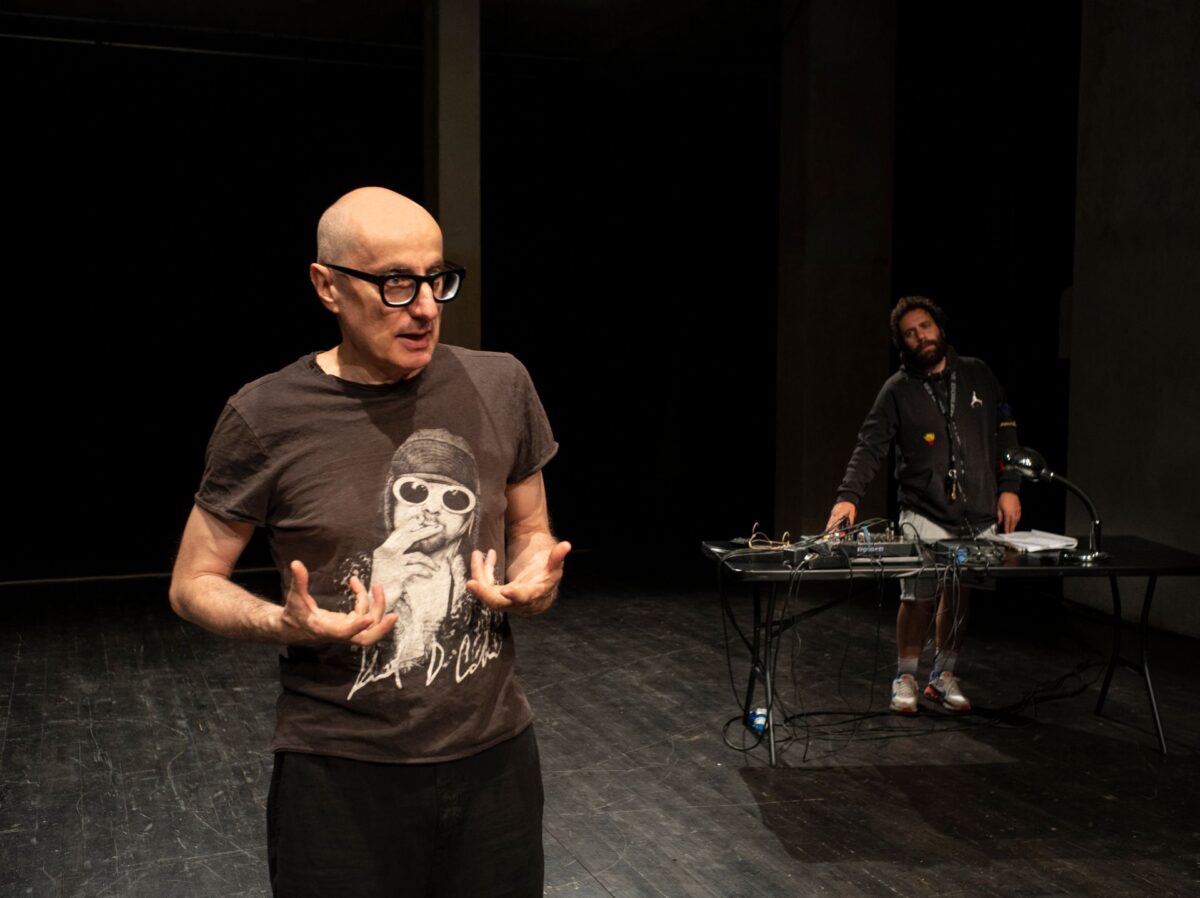 Un attore in primo piano rivolge il suo racconto al pubblico, sul fondo il musicista crea il paesaggio sonoro con un set per dj, nelle prove dello spettacolo Anton Cechov Remix