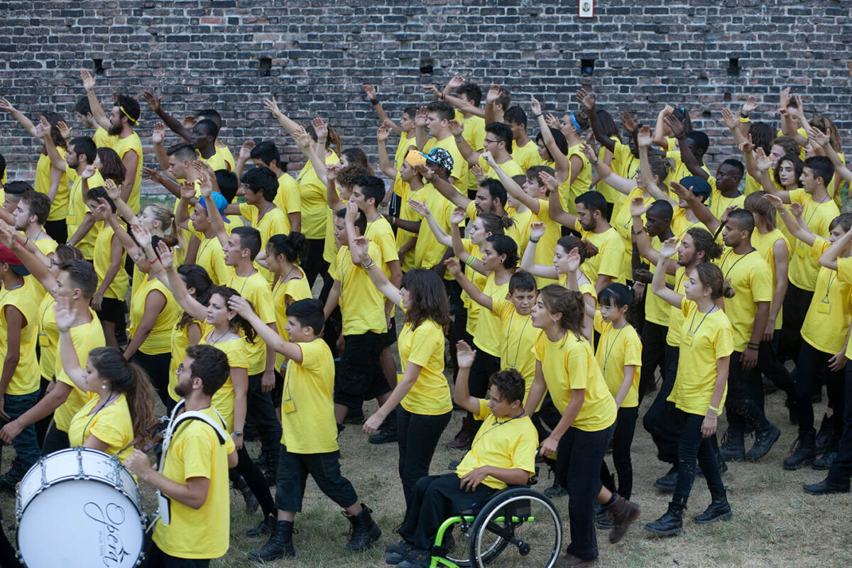 Coro di giovani in maglietta gialla in un’azione collettiva dello spettacolo Eresia della felicità a Milano nel 2015