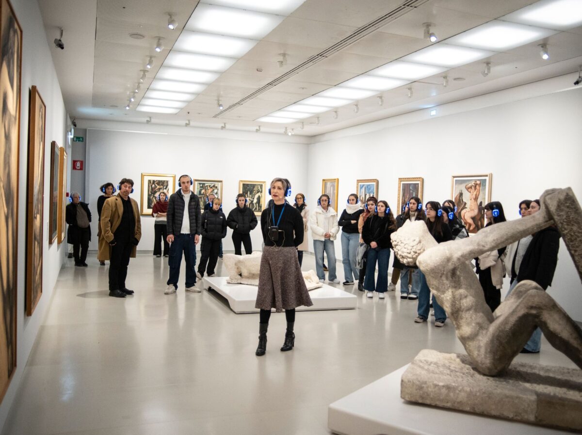 Un gruppo di studentesse e studenti ascolta in cuffia, di fronte alle opere d'arte esposte, Roberta Bosetti, nella performance itinerante al Museo del Novecento dal titolo Exhibition