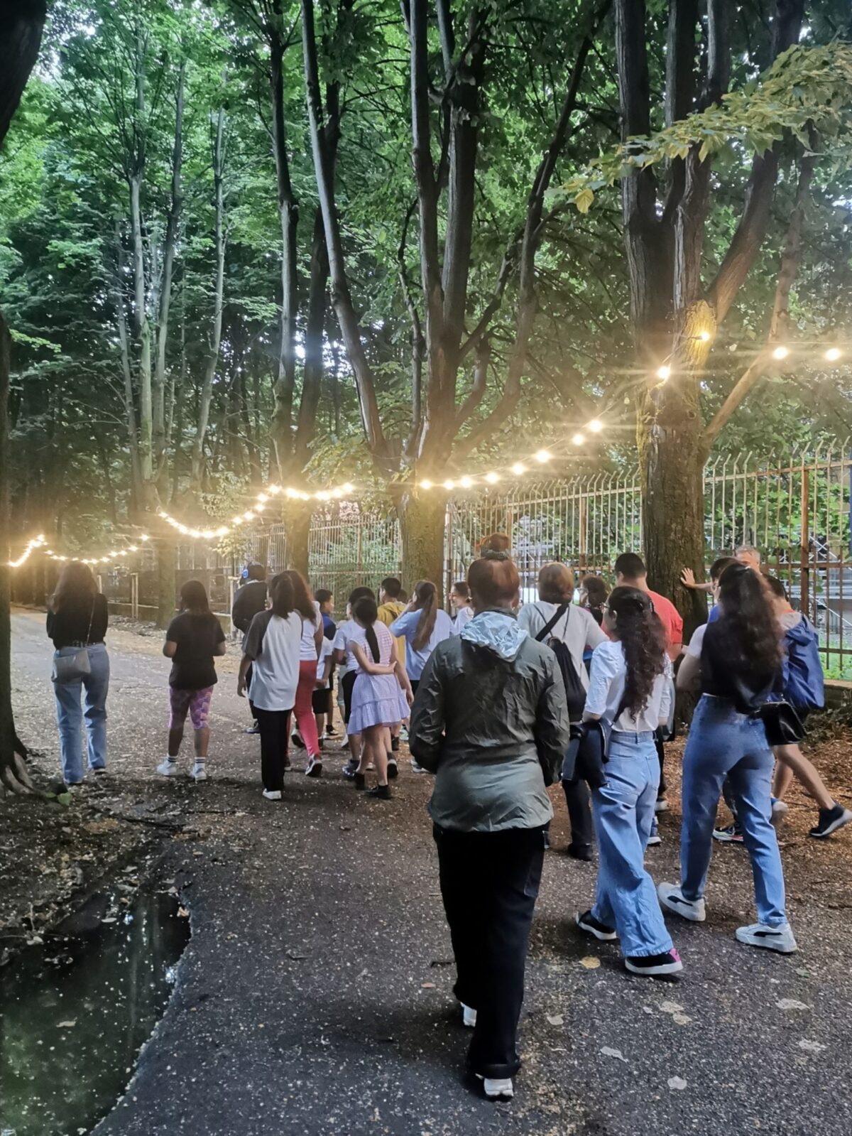 Un gruppo di bimbe e bimbi in cammino su un viale illuminato e alberato per la performance itinerante nel parco Hansel e Gretel