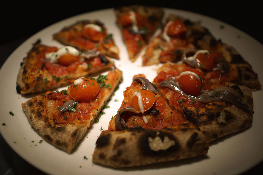 Pizza artigianale con pomodorini, acciughe e crema leggera, servita al ristorante Jodok.