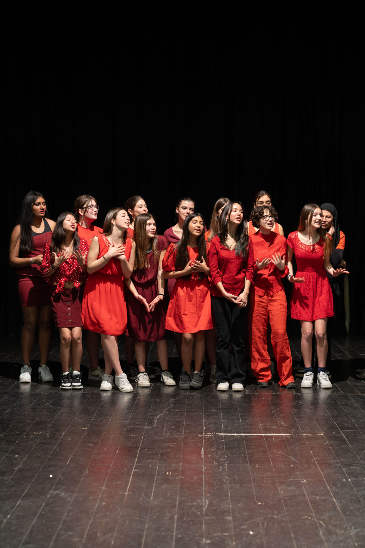 Ragazze e ragazzi in scena con abiti rossi e bordeaux, durante una restituzione pubblica del progetto non-scuola al TeatroLaCucina.