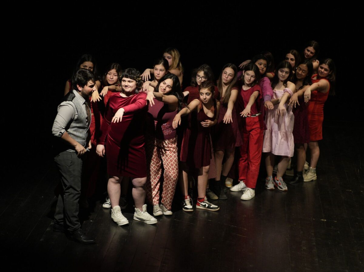 Giovani ragazze vestite di rosso mostrano le mani senza anello a un ragazzo con completo elegante, nell'esito pubblico del laboratorio di teatro con adolescenti non-scuola, liberamente tratto da L'opera da tre soldi di Brecht