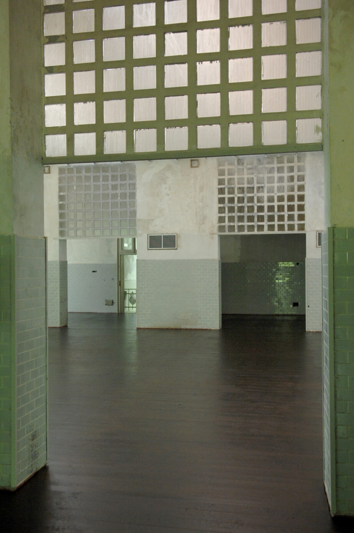 Vista dal corridoio della sala del teatrolacucina, con archittetura industriale e piastrelle in ceramica verde della ex mensa dell'ospedale psichiatrico