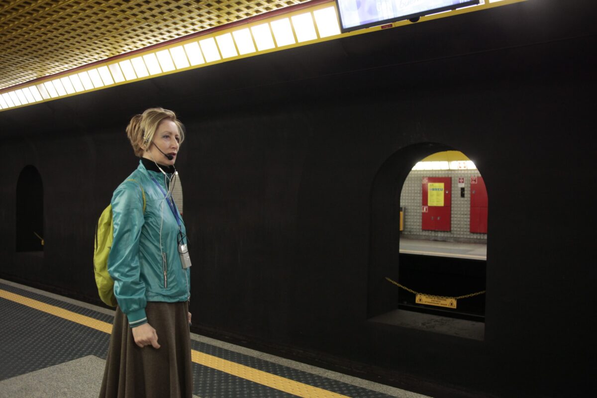 Performance itinerante nella metropolitana di Milano, dallo spettacolo Underground (2019), con interprete in cuffia e microfono nella stazione.
