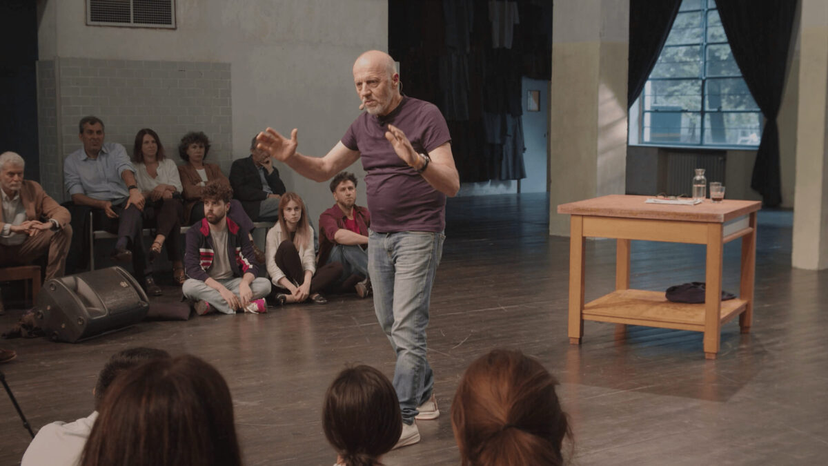 Marco Paolini in scena al TeatroLaCucina durante lo spettacolo VajontS 23 (2023), con il pubblico raccolto intorno in un’atmosfera intima e partecipata.
