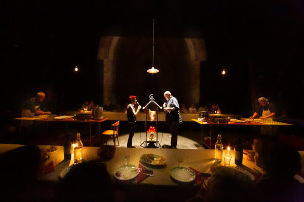 Un uomo e una donna stanno di fronte a due leggi illuminati guardandosi negli occhi, intorno a formare un quadrato la tavola imbandita e apparecchiata