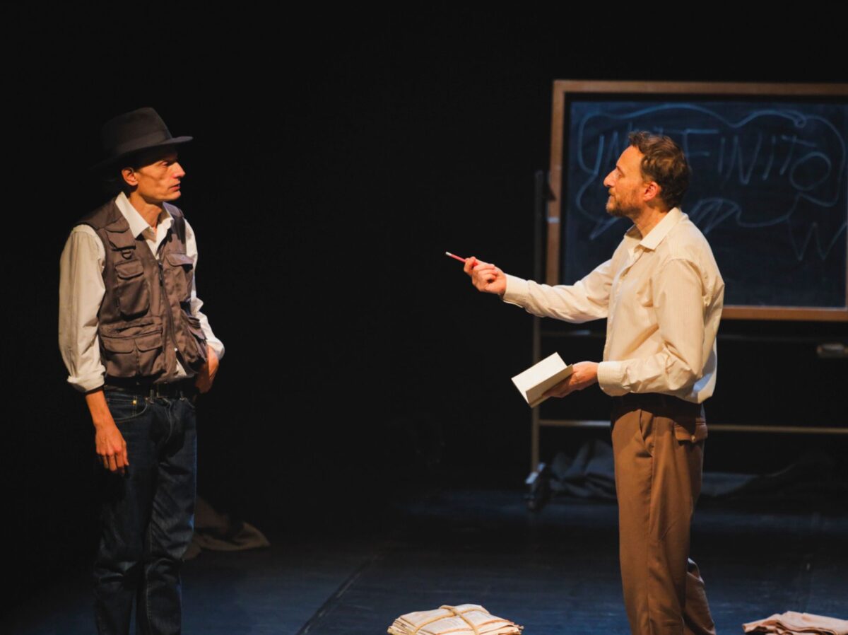 Sulla sinistra l'attore che interpreta Beuys, sulla destra l'altro attore che riveste la parte dell'intervistatore, con un taccuino in una mano e nell'altra una penna rivolta verso beuys, per prendere appunti