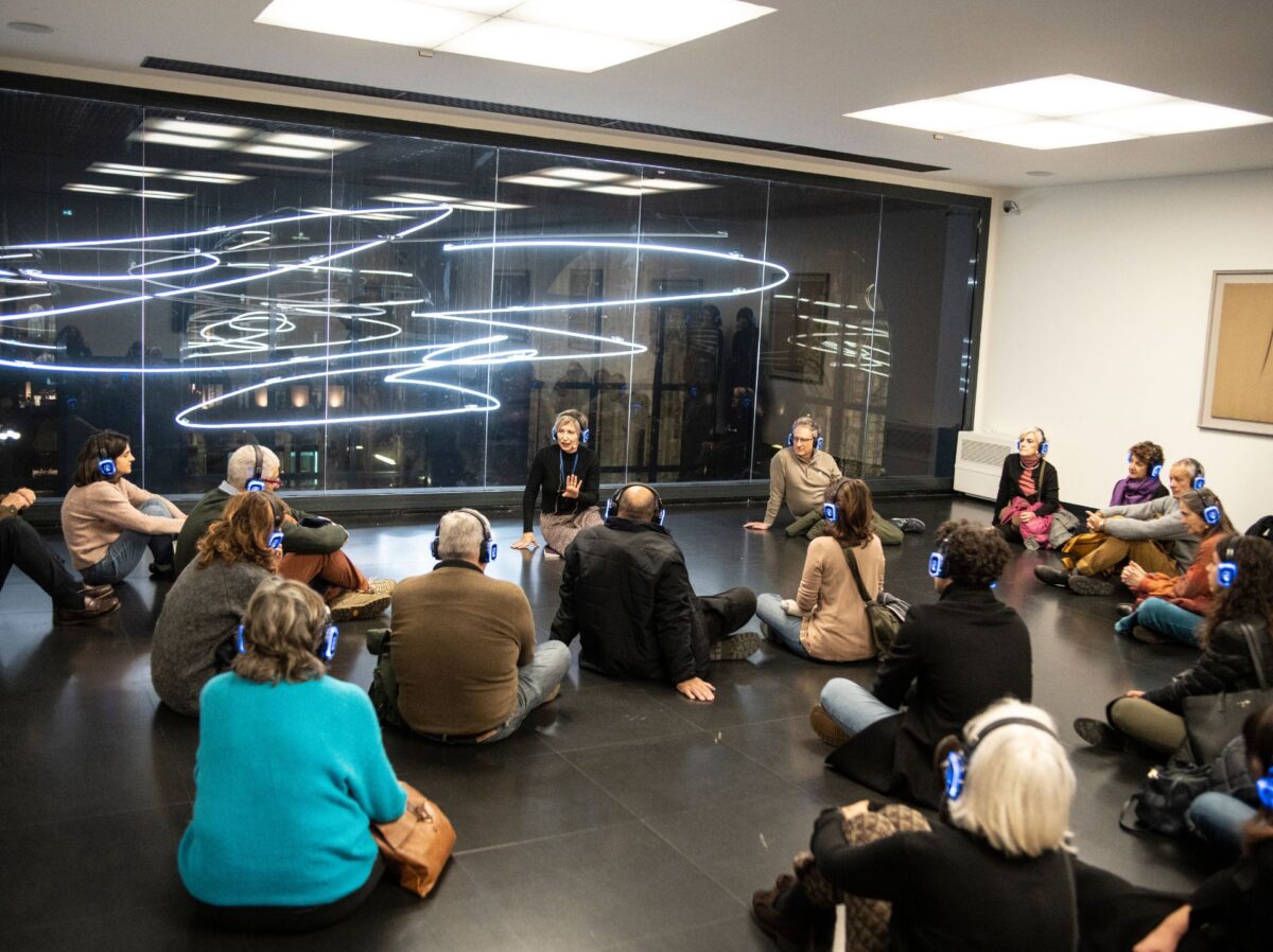 l'attrice sta seduta nella sala del museo del novecento dedicata a fontana, il pubblico di fronte a lei munito di cuffie sta in ascolto