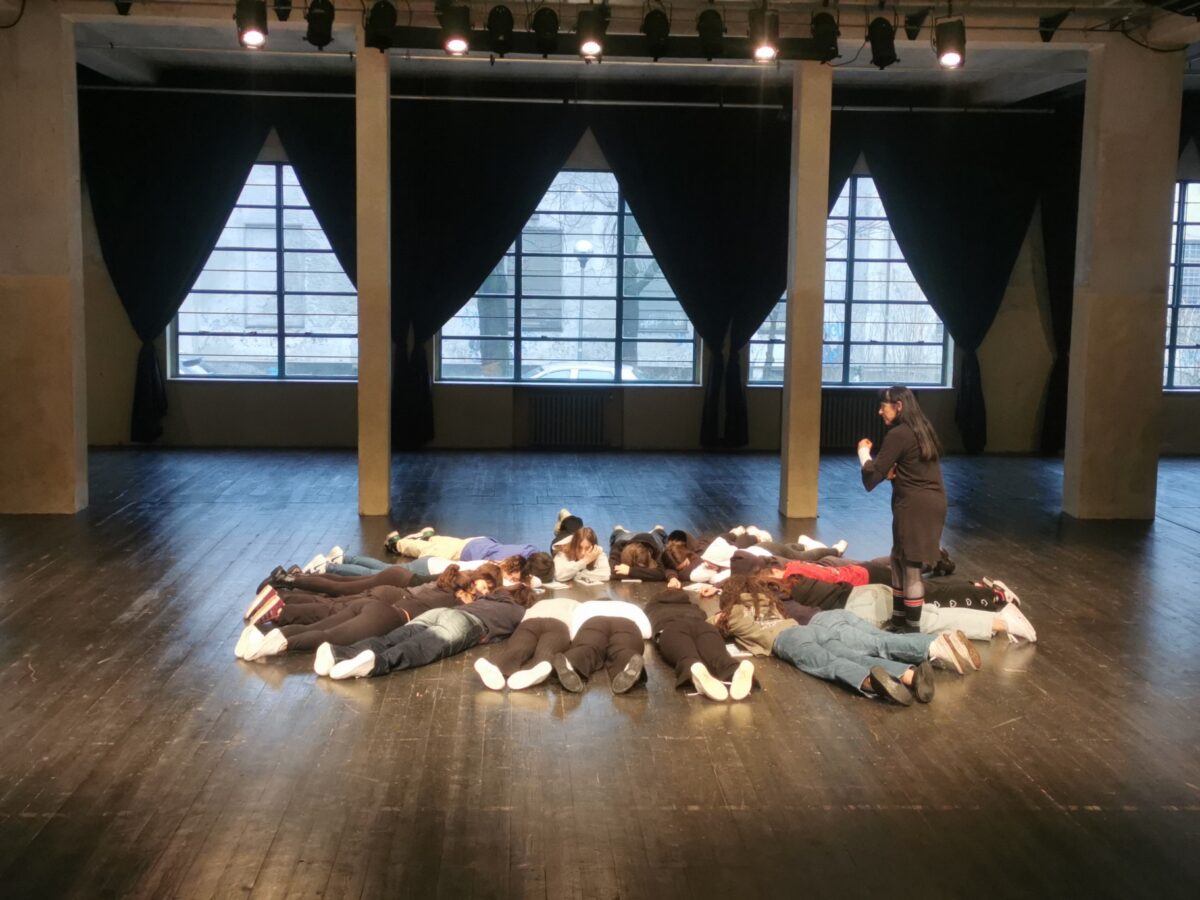 un gruppo di adolescenti sta in cerchio, sdraiato a pancia in sotto, sul palco del teatrolacucina, ex mensa dell'ex o.p. paolo pini, mentre la conduttrice del laboratorio dà istruzioni sugli esercizi di riscaldamento da svolgere