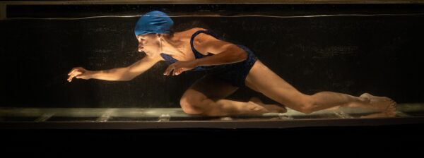 Una donna con cuffia e costume nuota in una vasca piena d'acqua, quasi alla ricerca di qualcosa, è l'attrice dell'installazione nodo in gola, gfabriella salvaterra