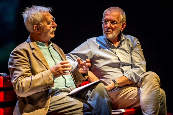 Due uomini, uno sulla 80ina e l'altro sulla 60ina, discutono seduti a una panchina sulla rivoluzione basagliana, che nel 1978 ha chiuso i manicomi in italia, primo paese al mondo