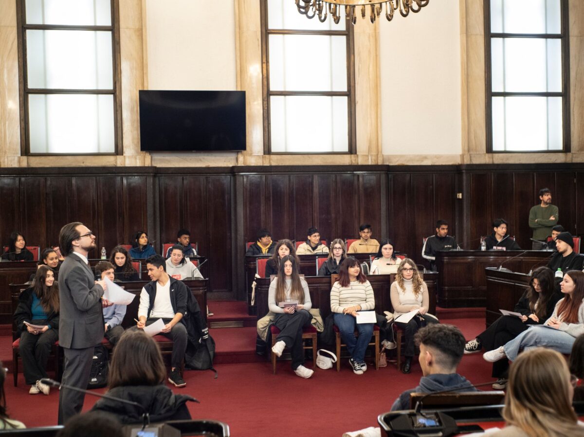 A lato dell'aula consigliare di palazzo marino, l'attore che interpreta primo levi, seduti sugli scranni dei consiglieri studenti e studentesse di quinta superiore