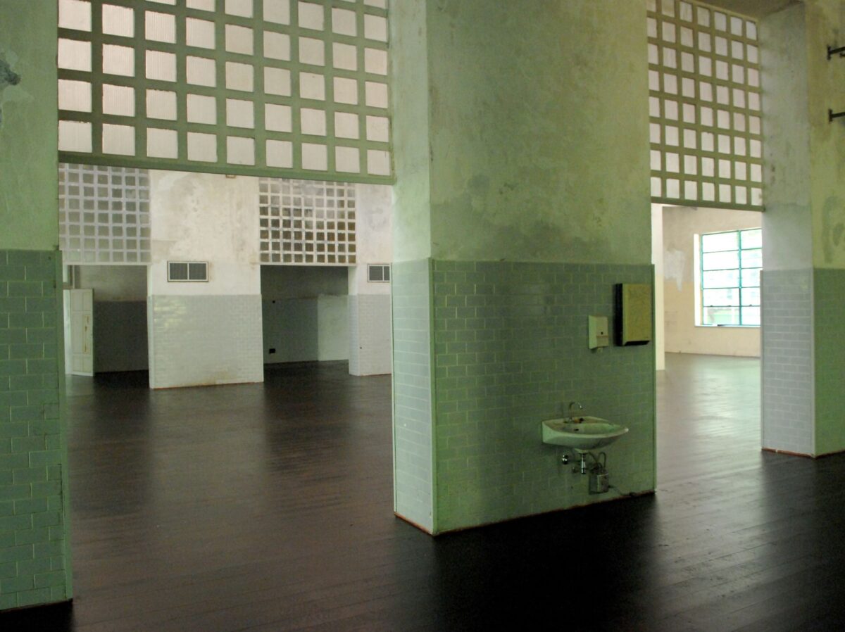 Corridoio del TeatroLaCucina, ex mensa dell'ospedale psichiatrico, con architettura industriale e un lavabo e piastrelle color verde